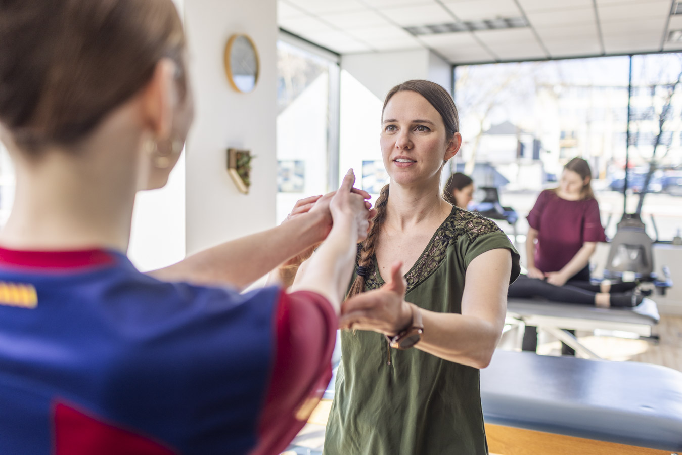 A physical therapist works with a patient. The photo composition shows the dancer's back, arms to head. The dancer's arms are held out and palms are together, the therapist holds up her arms and provides treatment.